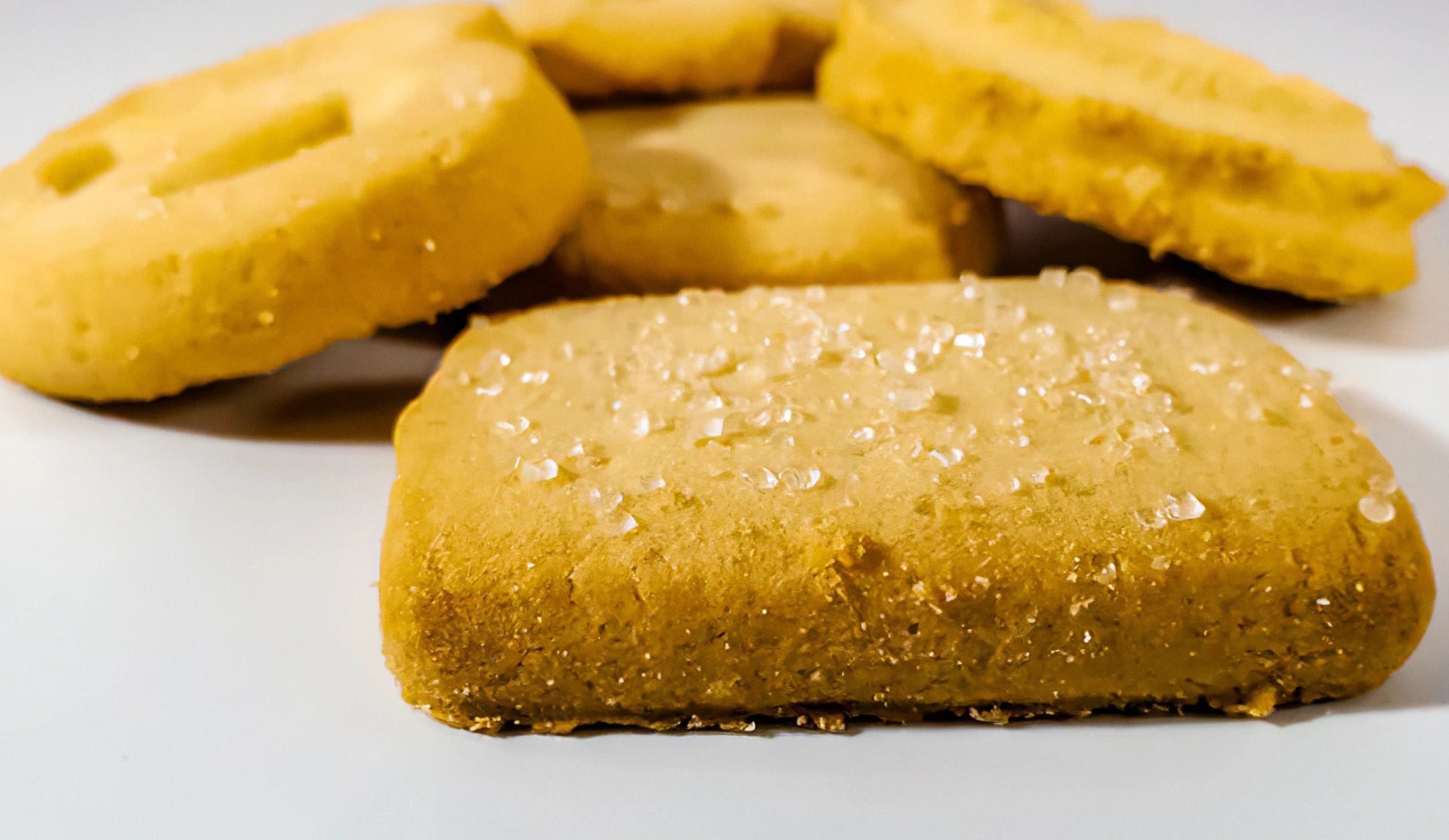 Homemade shortbread cookies, possibly flavored with vanilla, arranged on a white background. The focus is on a square cookie with a dusting of sugar, suggesting a crumbly and buttery texture.
