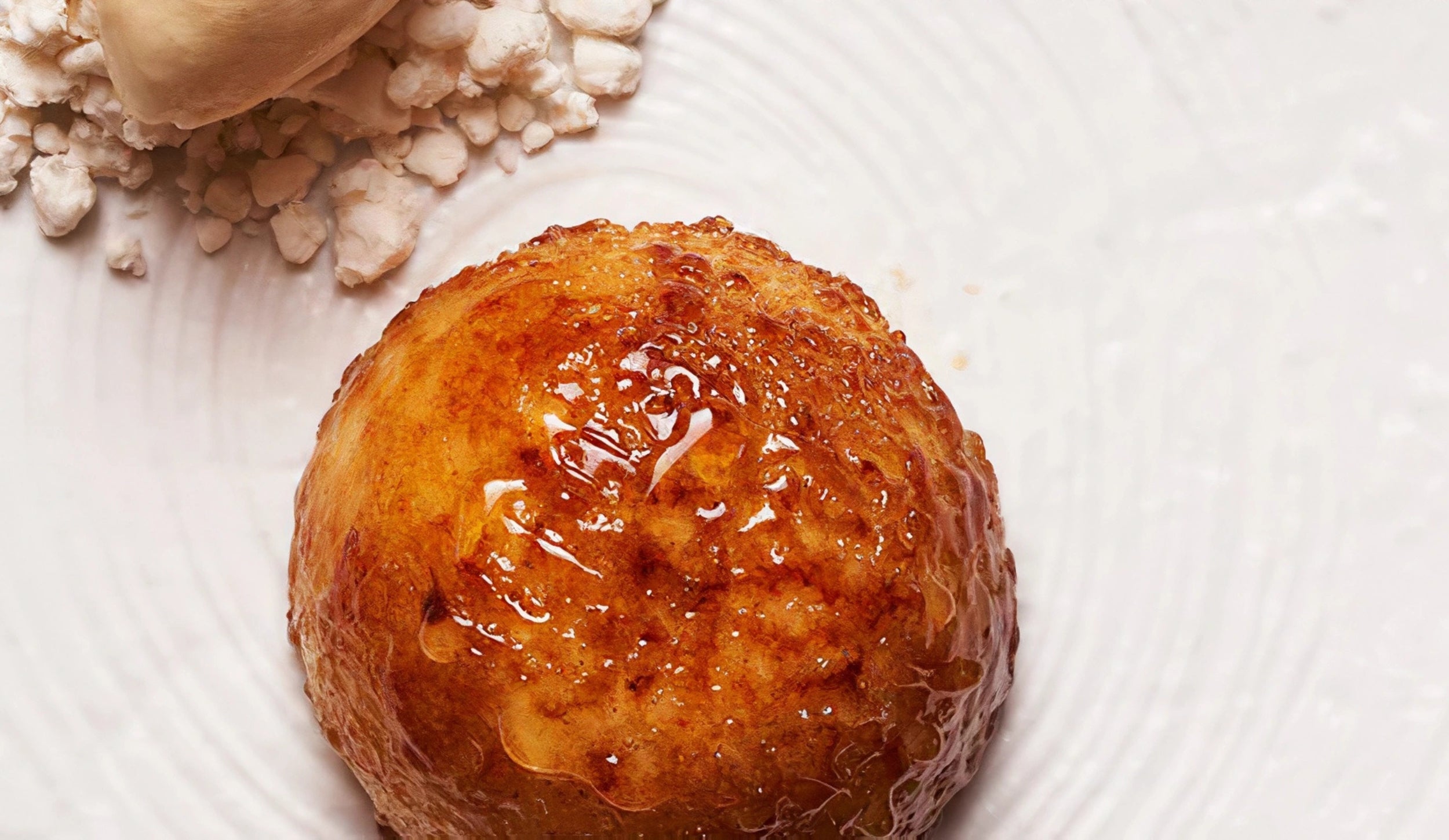 Golden sponge cake dessert with syrup, ice cream, and crumbs on a white plate.
