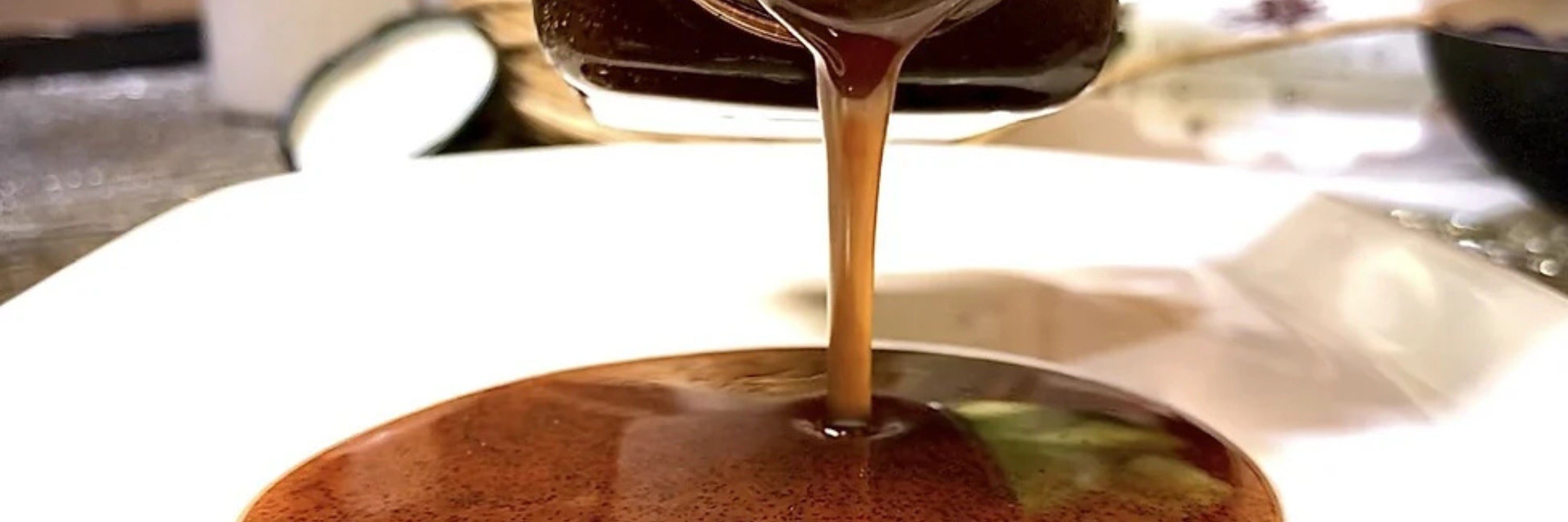 A thick, dark brown vanilla bean paste being poured from a jar into a white dish. The paste has a rich texture with visible vanilla seeds.