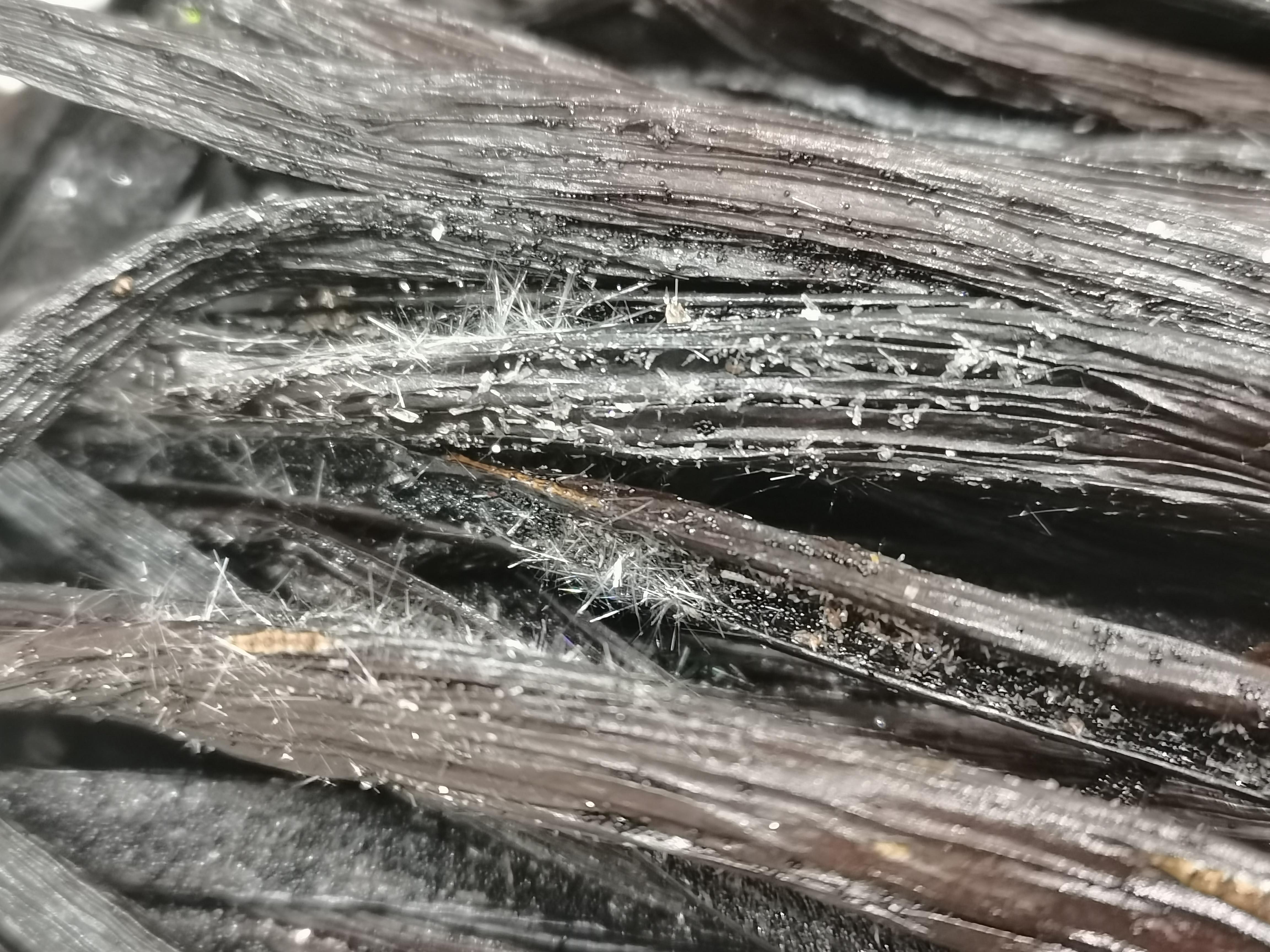 A close-up shot of Crystal Vanilla beans, showcasing their dark brown color and the delicate, frosty vanillin crystals forming on their surface.